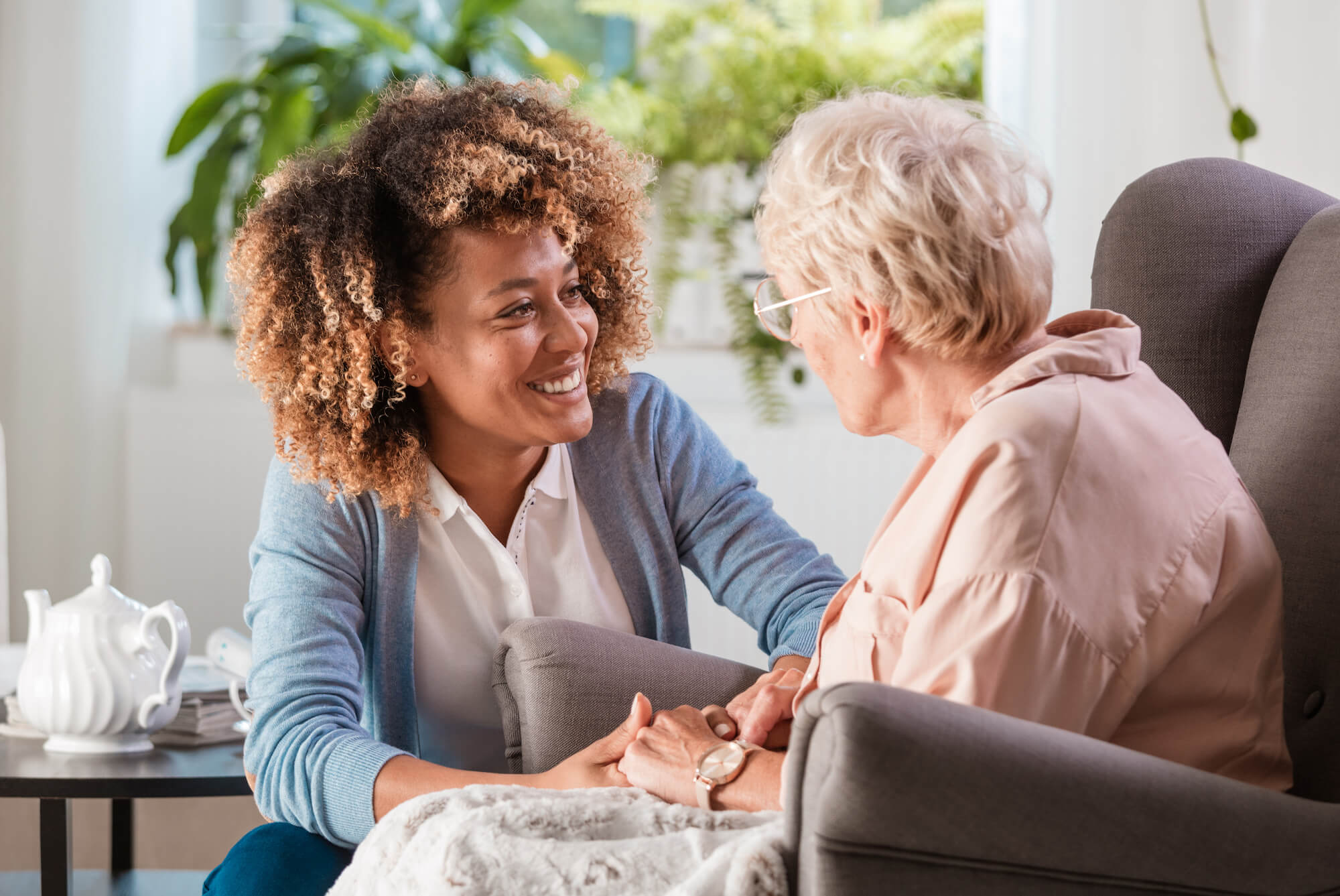 Female home caregiver talking with senior woman, sitting in living room and listening to her carefully.